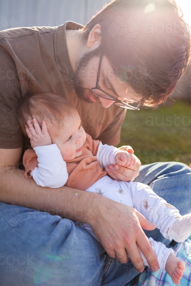 Young dad with happy tired baby outside in backyard - Australian Stock Image