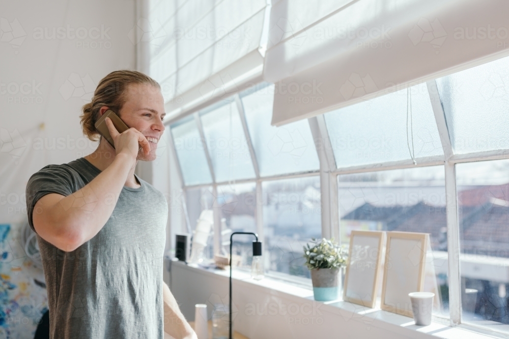 Young designer happily chatting on the phone in his studio - Australian Stock Image