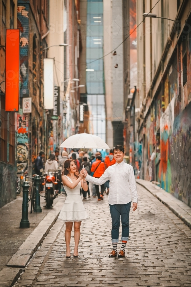 Young engaged couple posing with white umbrella in Hosier Lane, iconic graffiti laneway in Melbourne - Australian Stock Image