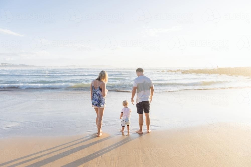 Young family of three standing on the beach at sunrise - Australian Stock Image