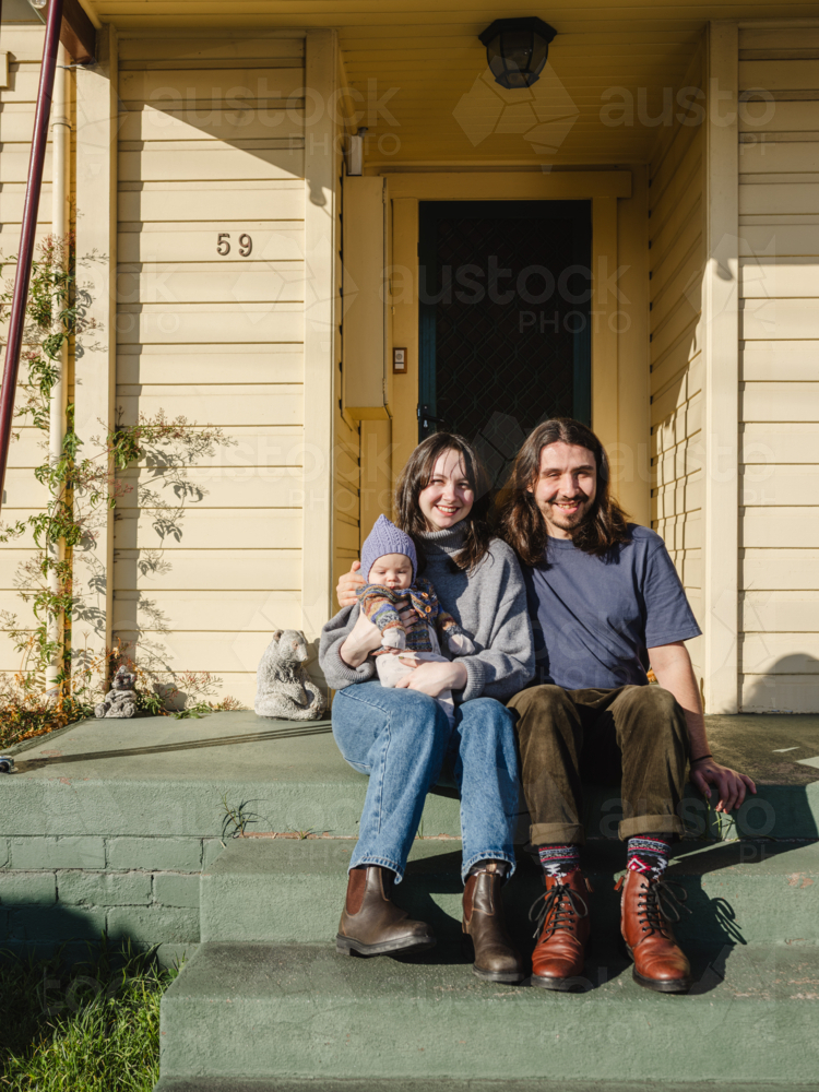 Young family sitting on the steps of their porch on sunny day - Australian Stock Image