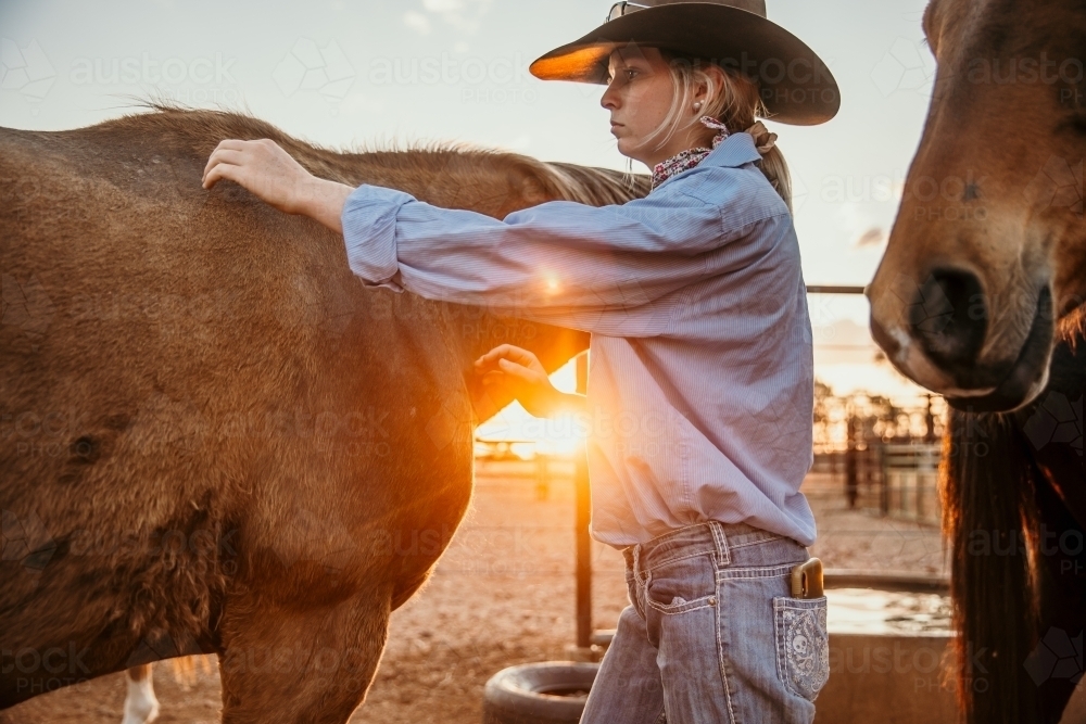 Young farm person patting horse at sunset - Australian Stock Image