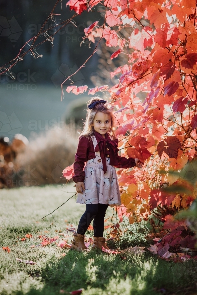 Young fashionable girl standing near autumn leavees smiling at camera - Australian Stock Image