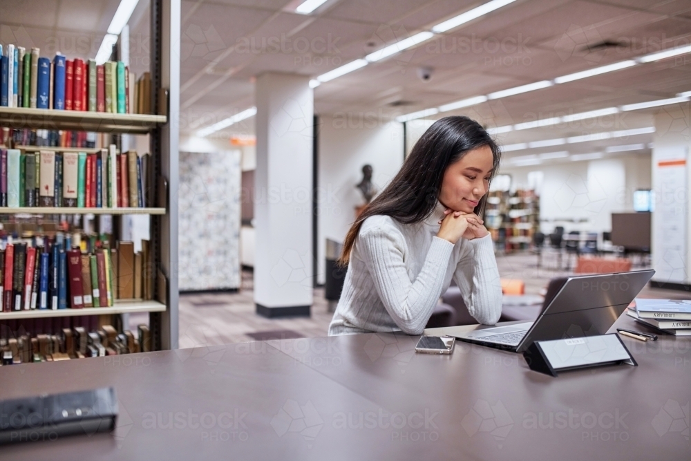 Young female Asian student working on her laptop at university library - Australian Stock Image