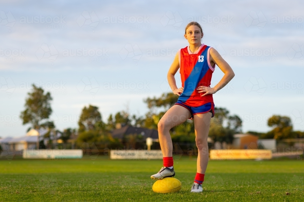 young female aussie rules footballer standing with hands on hips and foot on ball - Australian Stock Image