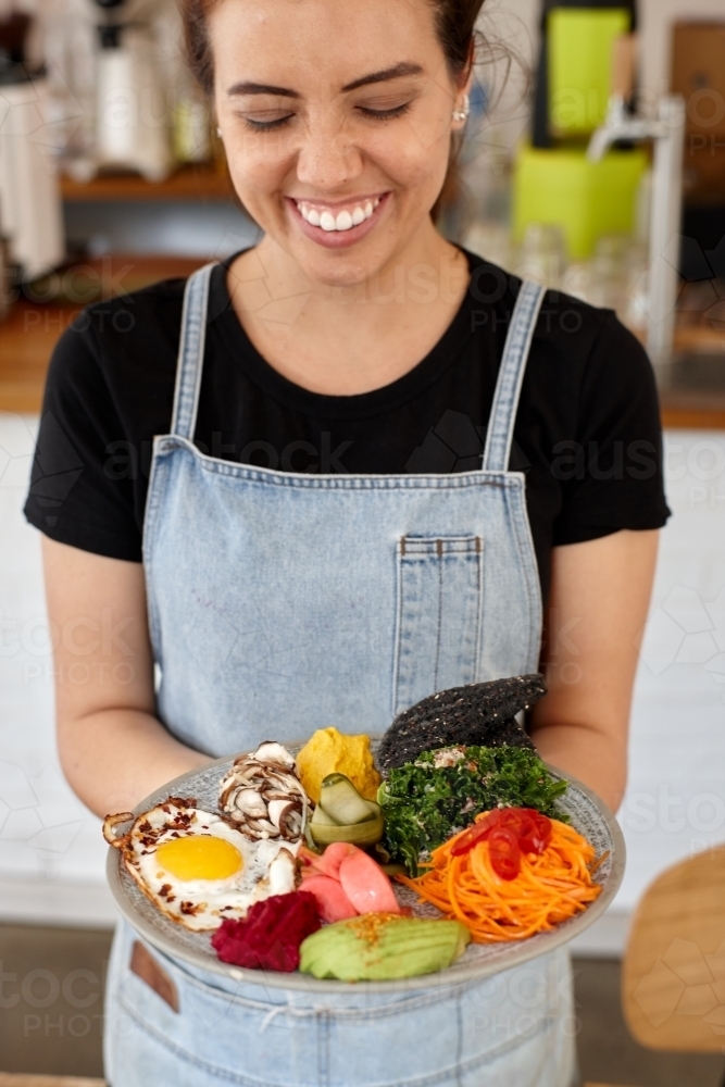 Young female cafe worker laughing holding healthy dish - Australian Stock Image