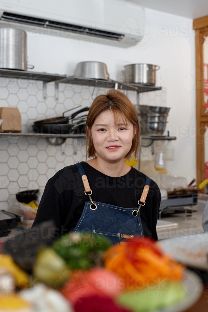 Young female chef in cafe kitchen preparing healthy vegetarian meal - Australian Stock Image