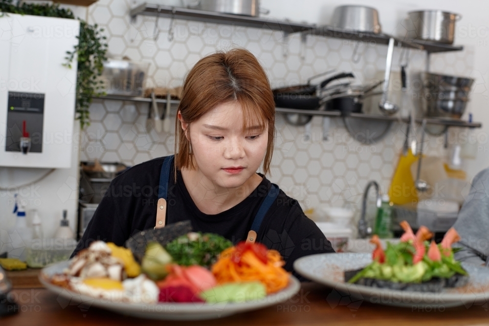 Young female chef in cafe kitchen preparing healthy vegetarian meal - Australian Stock Image