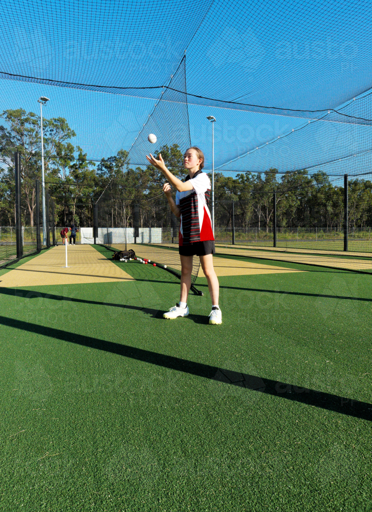 Young female cricketer practicing in the nets with a cricket ball - Australian Stock Image