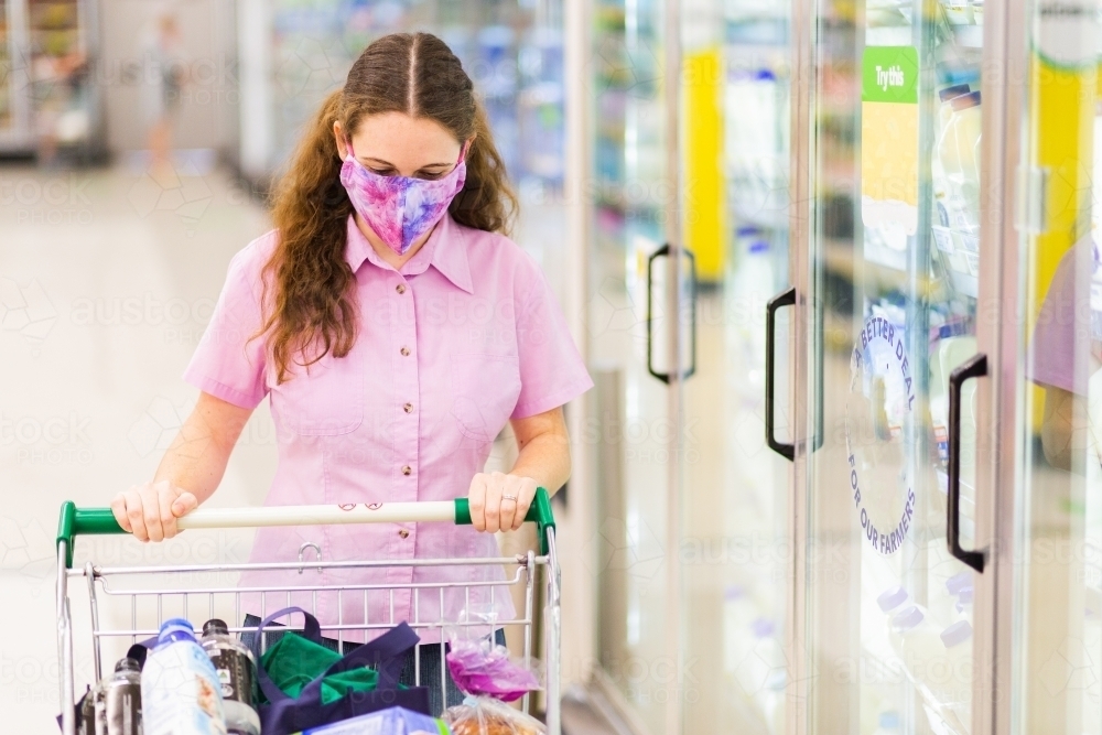 Young female shopper walking down grocery store aisle wearing home made face mask - Australian Stock Image