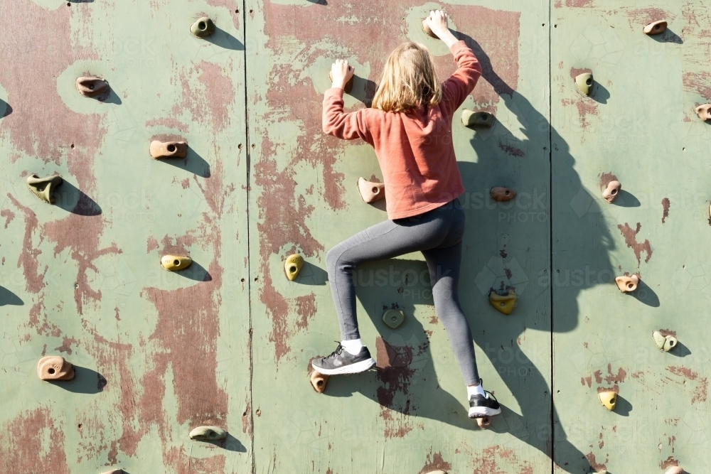 Young girl climbing a climbing wall in at a play ground on a sunny day - Australian Stock Image