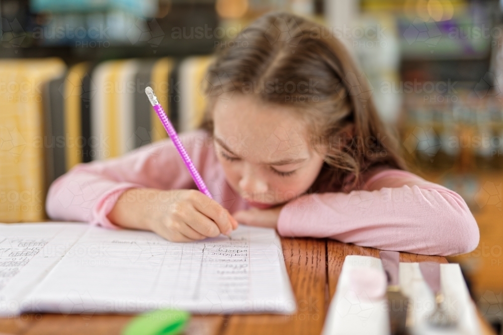 Young girl concentrating and writing in her homework book - Australian Stock Image