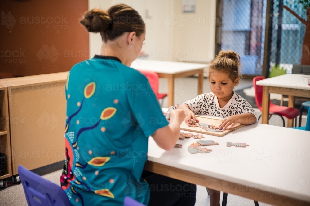 Young girl doing jigsaw puzzle with carer - Australian Stock Image