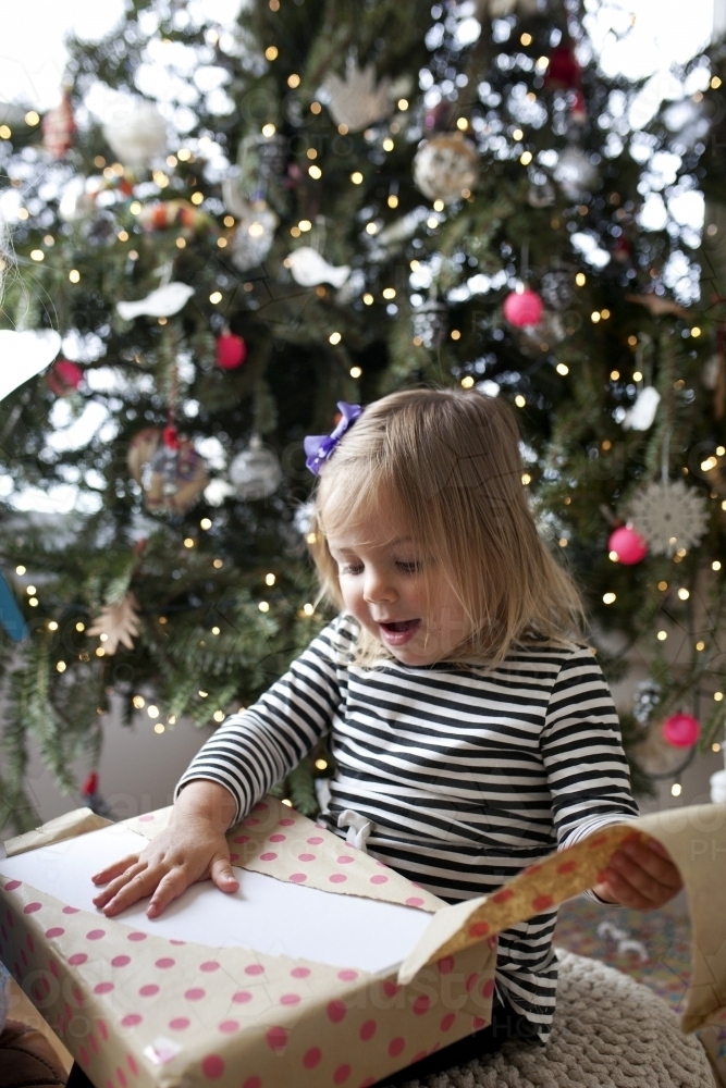 Young girl in front of Christmas tree opening a present - Australian Stock Image