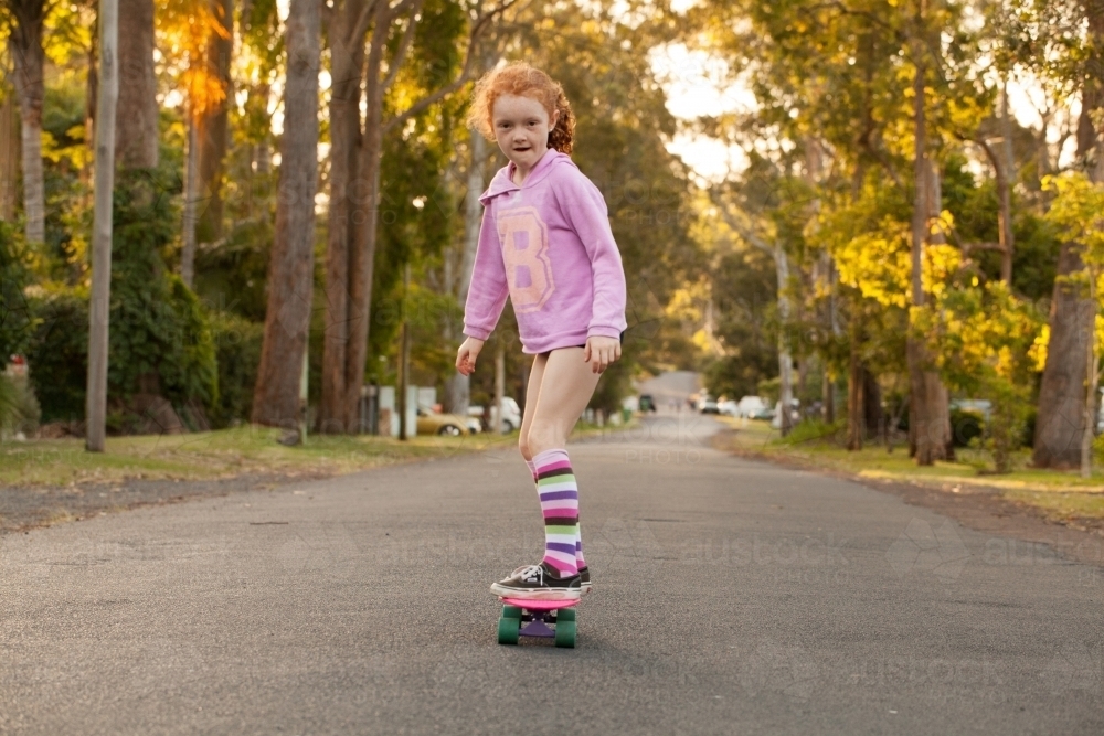 Young girl in long socks riding a skateboard along a road - Australian Stock Image