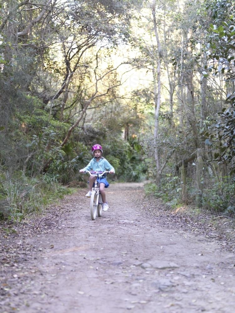 Young girl in purple helmet riding bike on bush track - Australian Stock Image