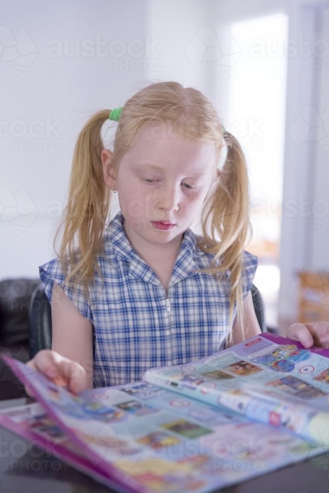 Young girl in school uniform reading a catalogue - Australian Stock Image