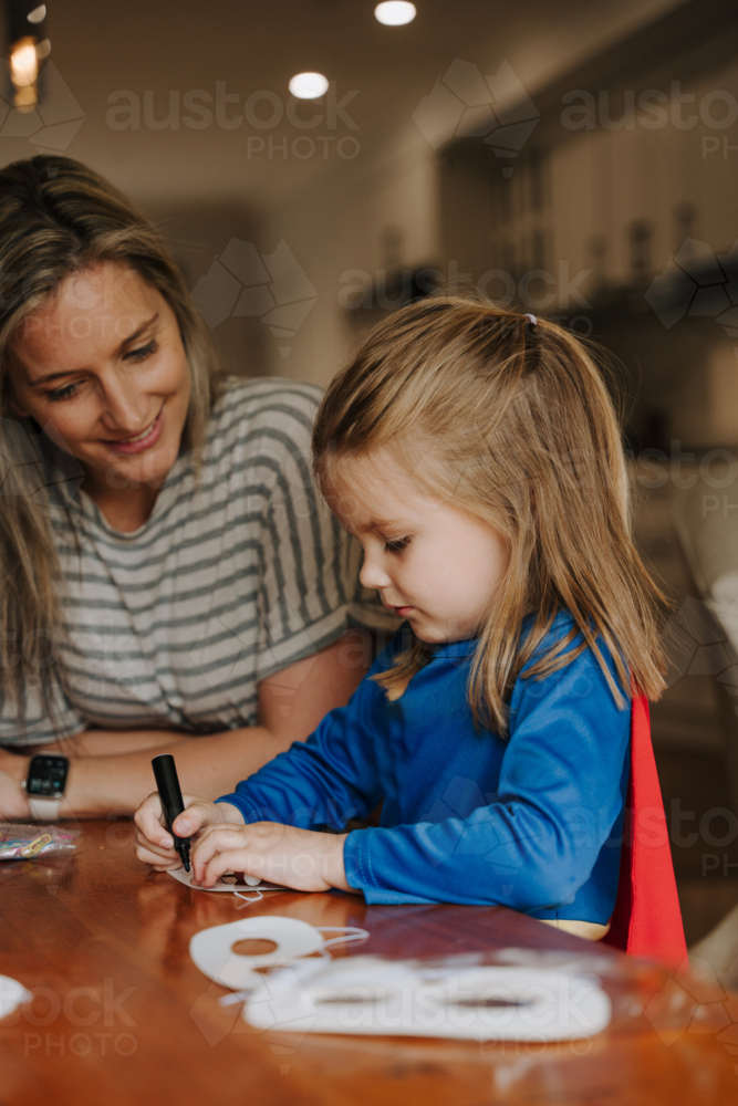 Young girl in superhero costume making and colouring her eyemask. - Australian Stock Image