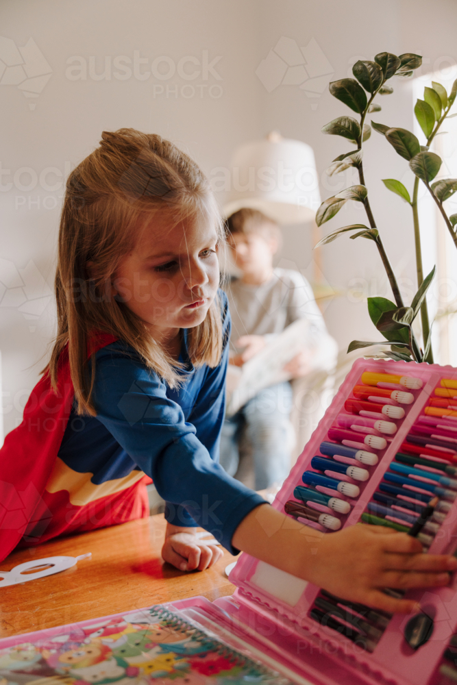 Young girl in superhero costume picking a colouring texta - Australian Stock Image