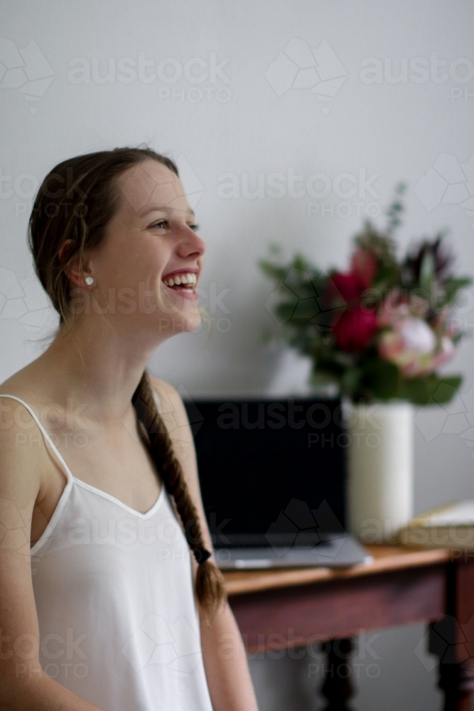 Young girl laughing inside in front of work desk - Australian Stock Image