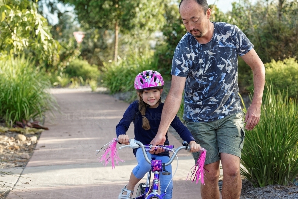 Young girl learning to ride her pushbike in the park with her dad - Australian Stock Image