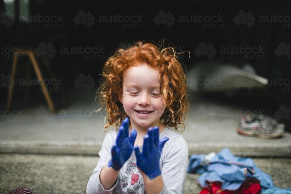 Young girl looking at her painted blue hands - Australian Stock Image