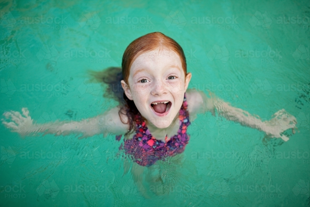 Young girl looking up from a pool smiling - Australian Stock Image