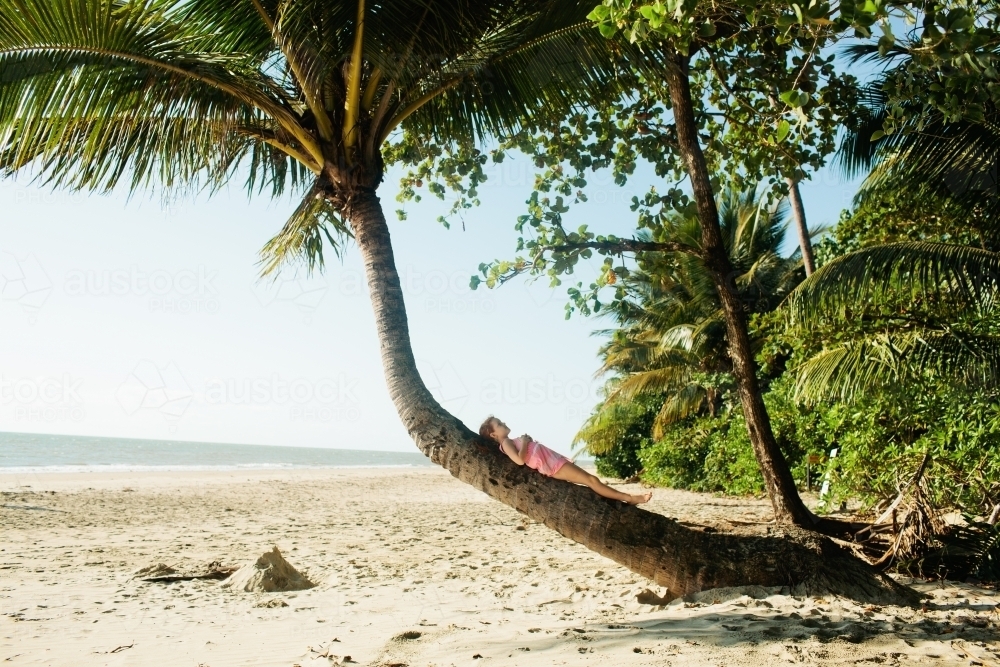 Young girl lying on a palm tree at the beach - Australian Stock Image