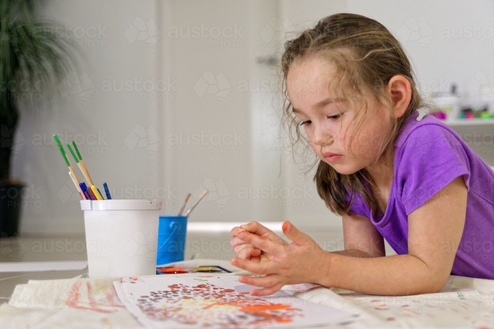 Young girl lying on the floor putting colour on her finger for painting a dot picture - Australian Stock Image