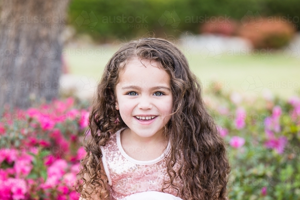 Young girl mixed race aboriginal and caucasian sitting in garden with flowers smiling - Australian Stock Image