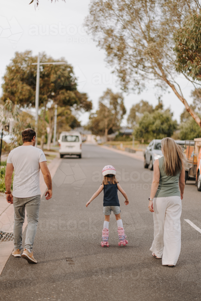 Young girl on roller blades with her parents on the street. - Australian Stock Image