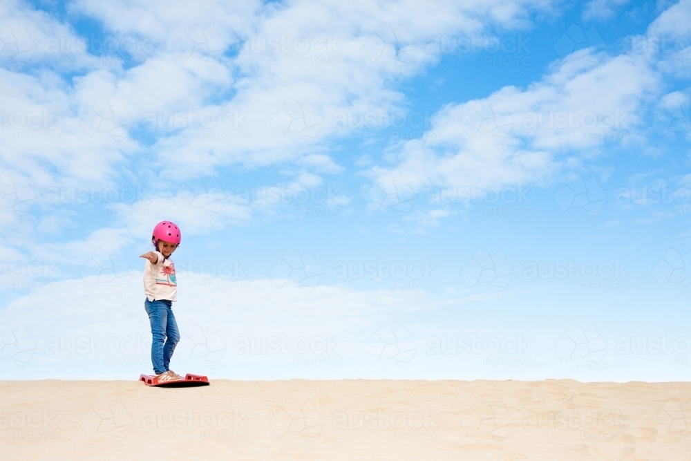 Young girl on top of sand dunes ready to sand board - Australian Stock Image