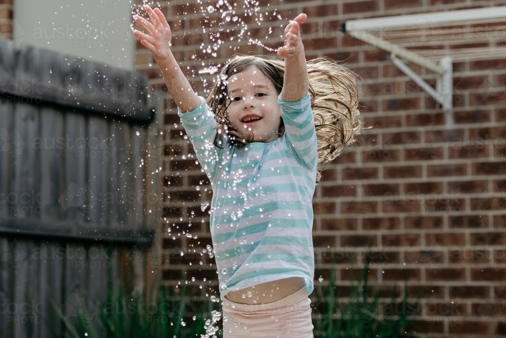 Young girl playing in home backyard splashing water - Australian Stock Image