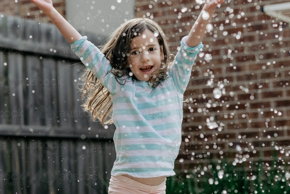 Young girl playing in home backyard splashing water - Australian Stock Image