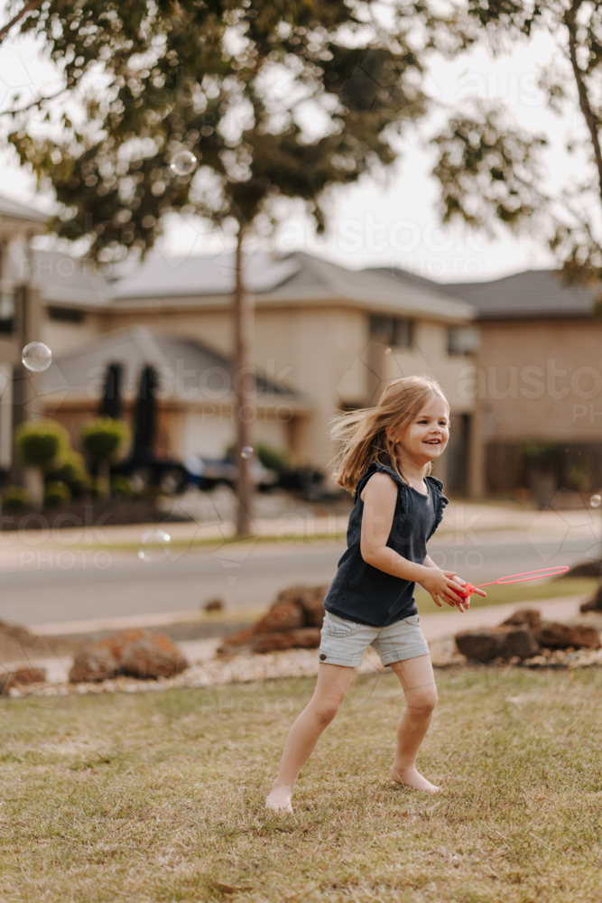 Young girl playing with bubbles in front yard. - Australian Stock Image