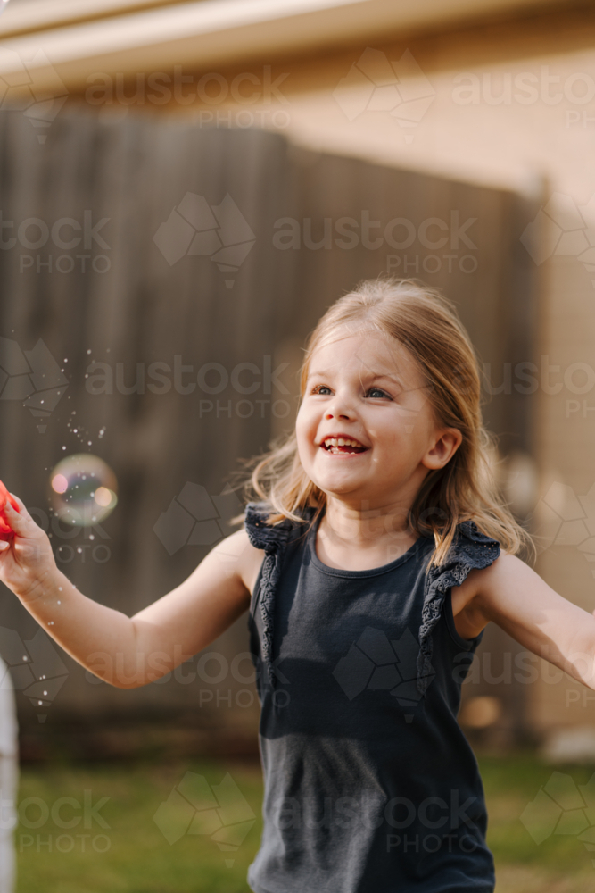 Young girl playing with bubbles inside their yard. - Australian Stock Image