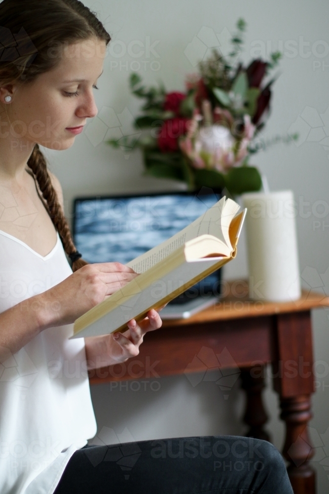 Young girl reading a book indoors by her work desk - Australian Stock Image