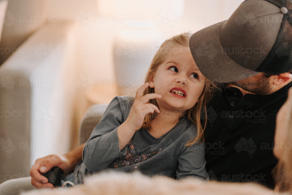 Young girl showing her teeth to her dad on the couch. - Australian Stock Image