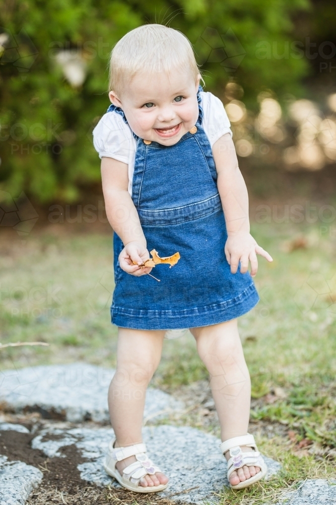 Young girl shrugging shoulders smiling holding leaf in garden - Australian Stock Image