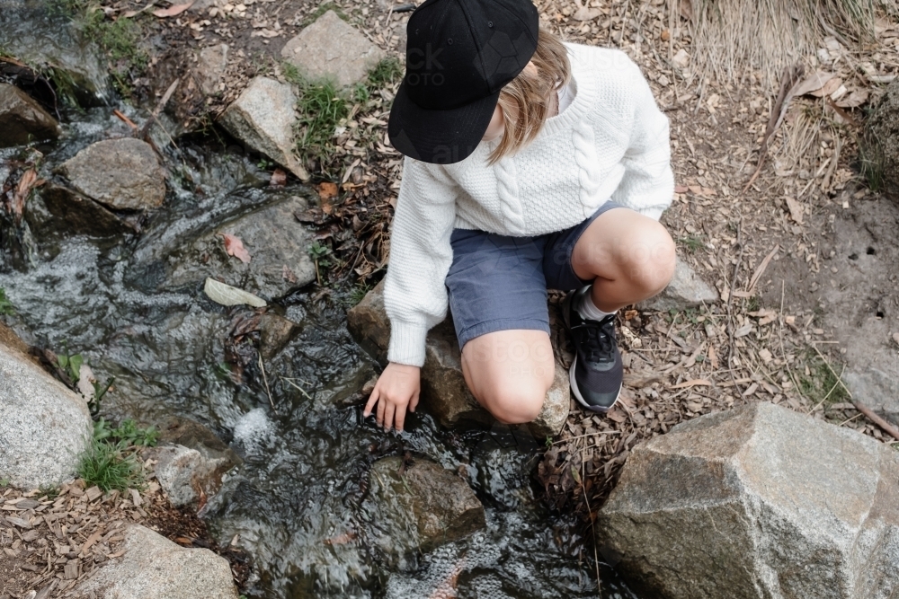 Young girl sitting by a creek touching the water - Australian Stock Image