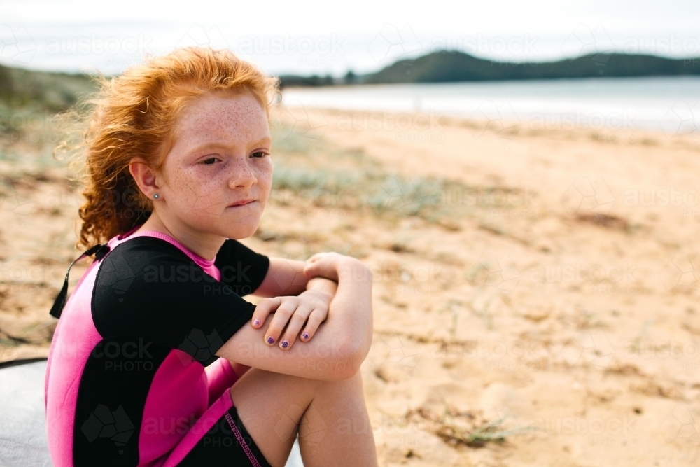 Young girl sitting on the beach looking sad - Australian Stock Image