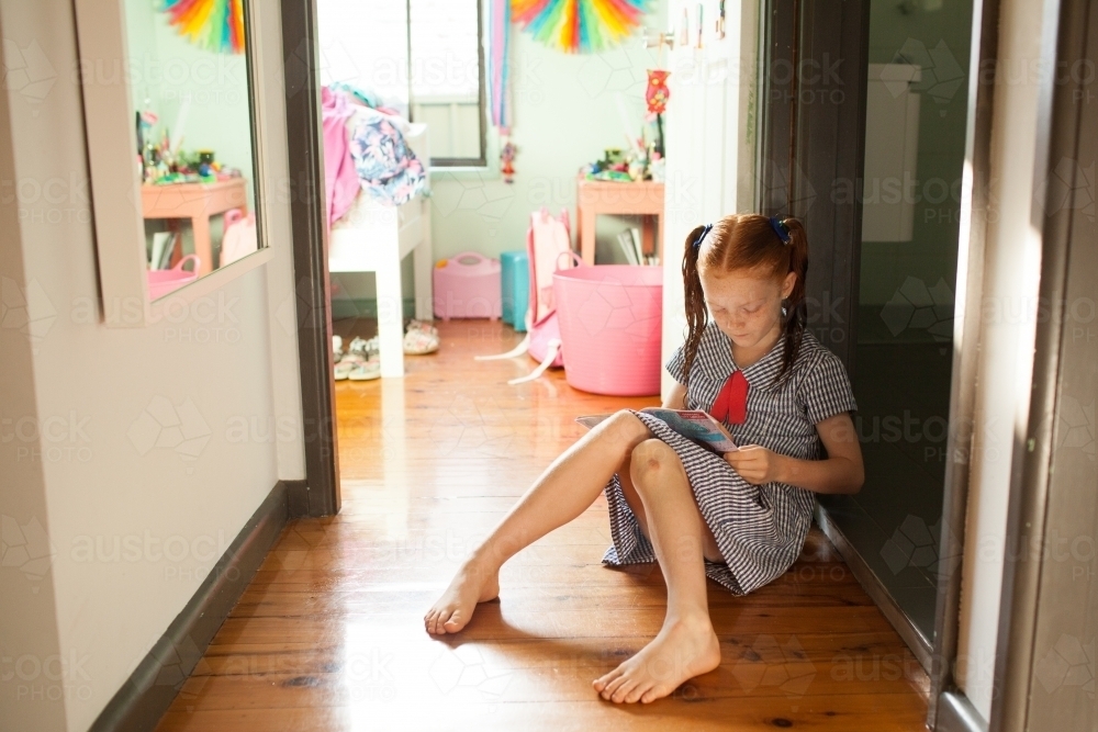 Young girl sitting on the floor reading a book - Australian Stock Image