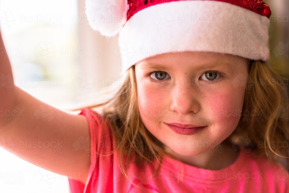 Young girl smiling and wearing a santa hat - Australian Stock Image