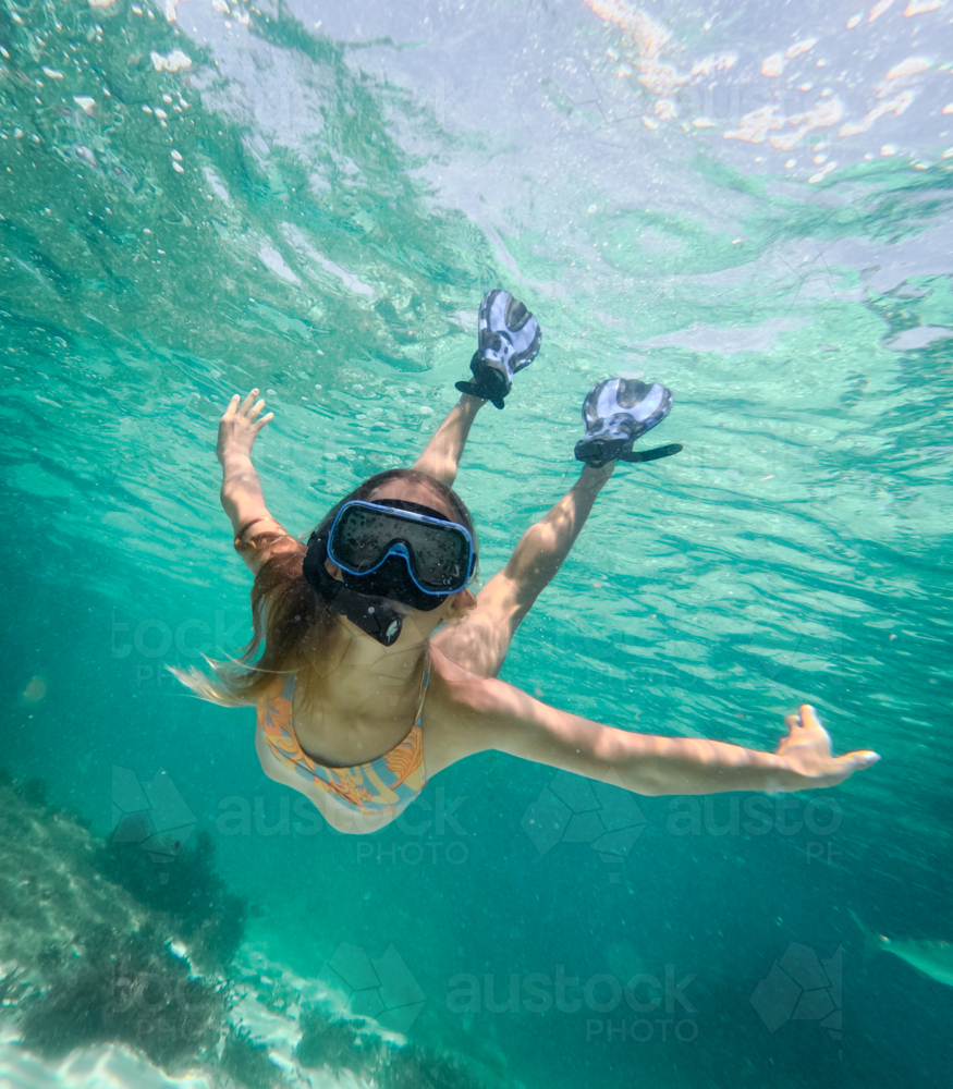 Young girl snorkelling diving down looking at camera in clear ocean - Australian Stock Image