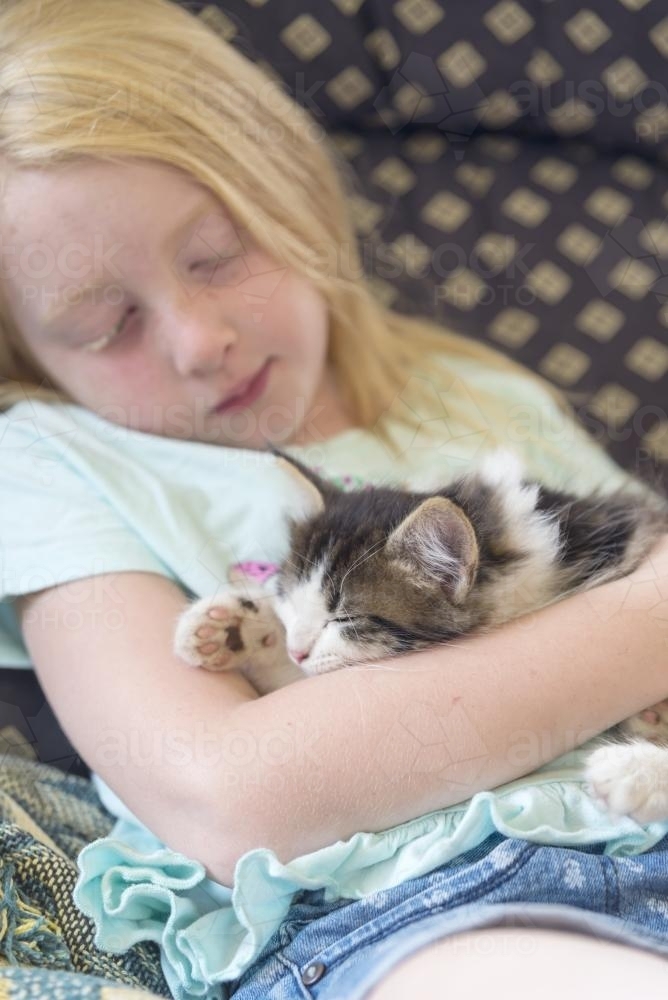 Young girl snuggling with sleeping rescue kitten - Australian Stock Image