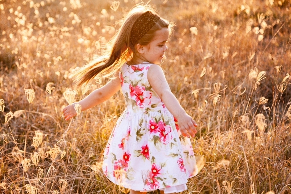 Young girl spinning in long grass, joy and sunlight - Australian Stock Image