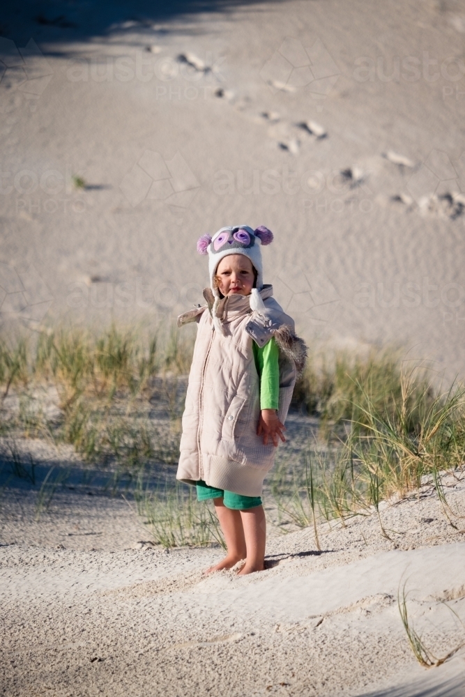 Young girl standing on dune dressed in oversized winter clothing - Australian Stock Image