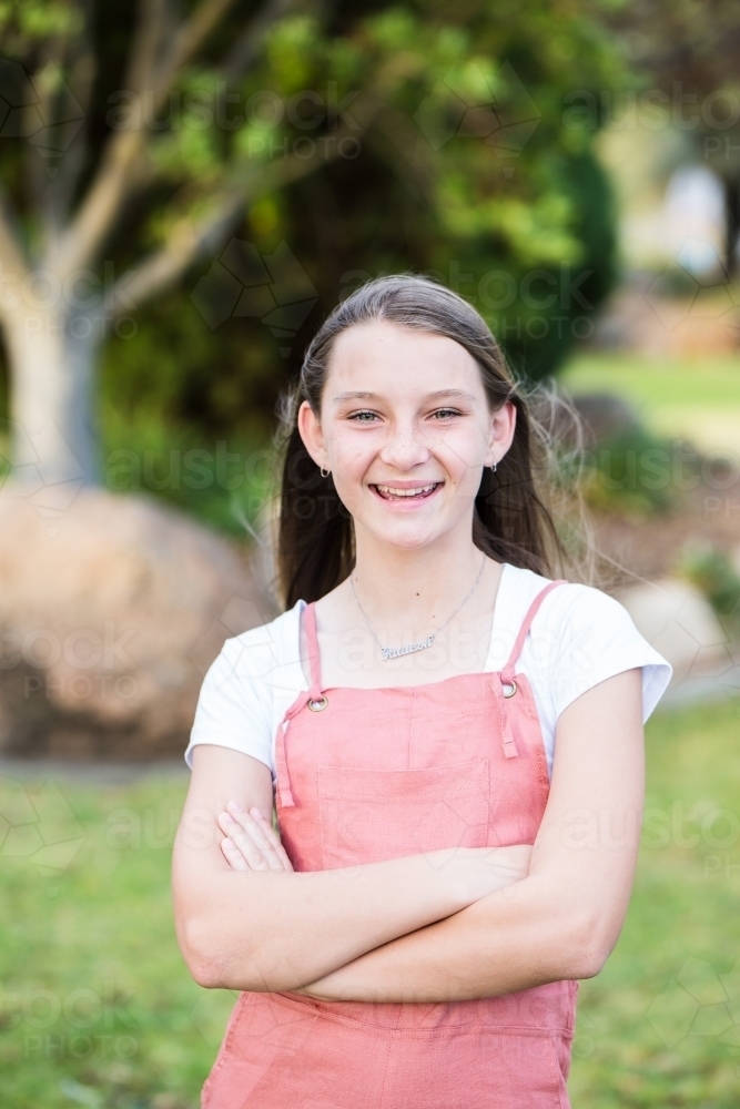 Young girl standing with arms crossed smiling in garden - Australian Stock Image