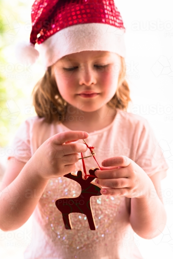 Young girl wearing a santa hat holding up a Christmas decoration - Australian Stock Image