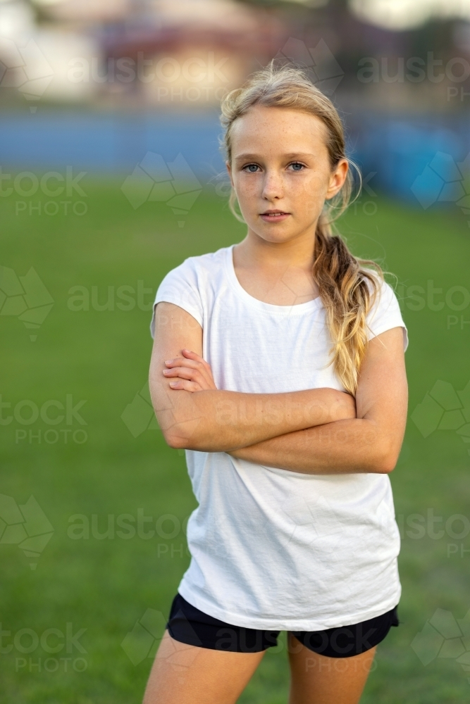 young girl wearing white tee shirt and black shorts standing with arms crossed - Australian Stock Image
